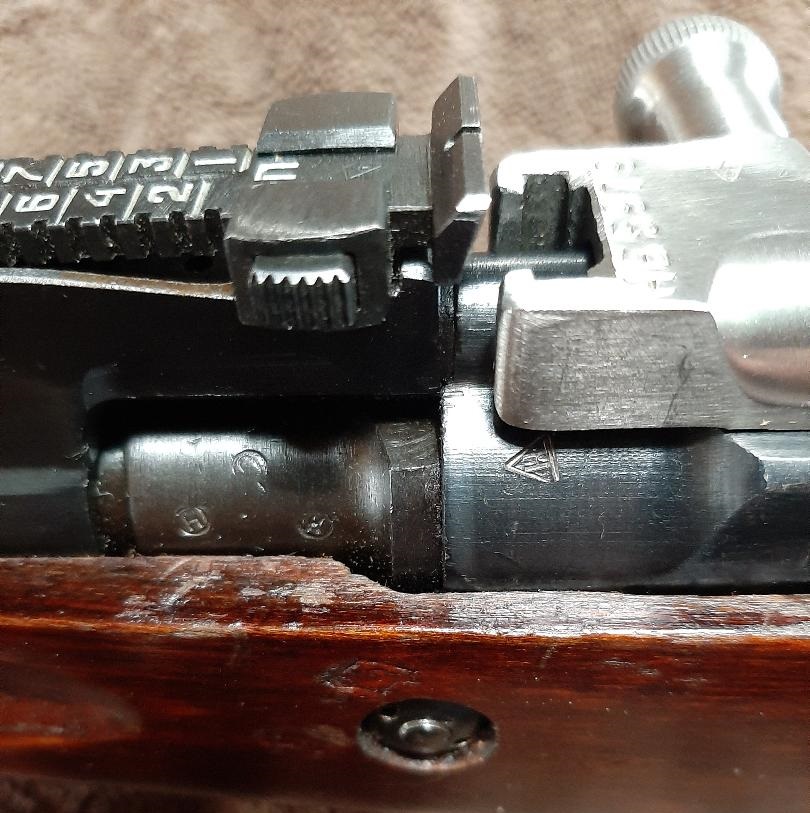 Close-up of rifle bolt and receiver with visible markings and rear sight
