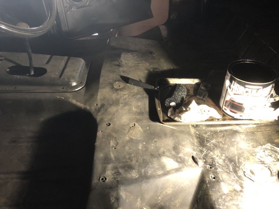 Vehicle floor with a knife, rag, and can of black paint. Someone is working on it