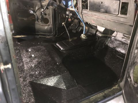 1978 Ford Bronco - The interior of a vehicle shows a black textured floor and dashboard with pedals and a gear shifter visible.
