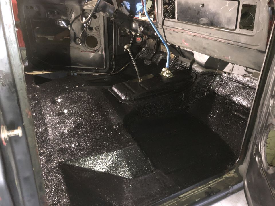 Black interior of a vehicle with a black textured floor and dashboard, showing pedals and a gear shifter