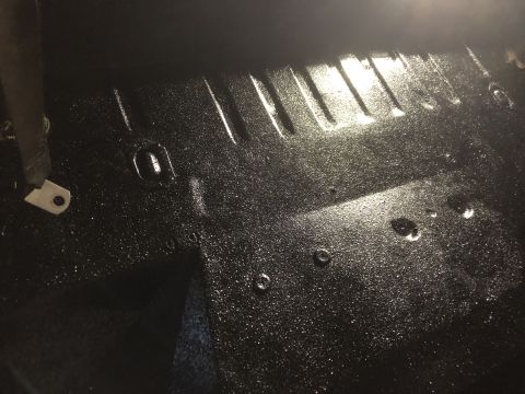 1978 Ford Bronco - Close-up view of the textured black floor pan inside a vehicle, showing a seatbelt anchor point.
