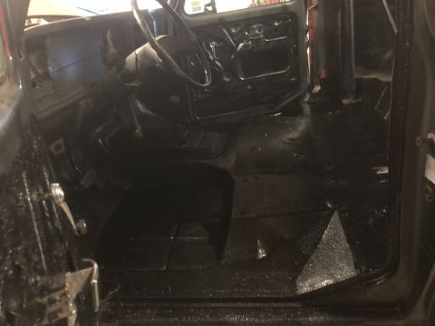 1978 Ford Bronco - The interior of a vehicle shows black textured flooring and the basic structure of the cabin, including the steering wheel and door frames.