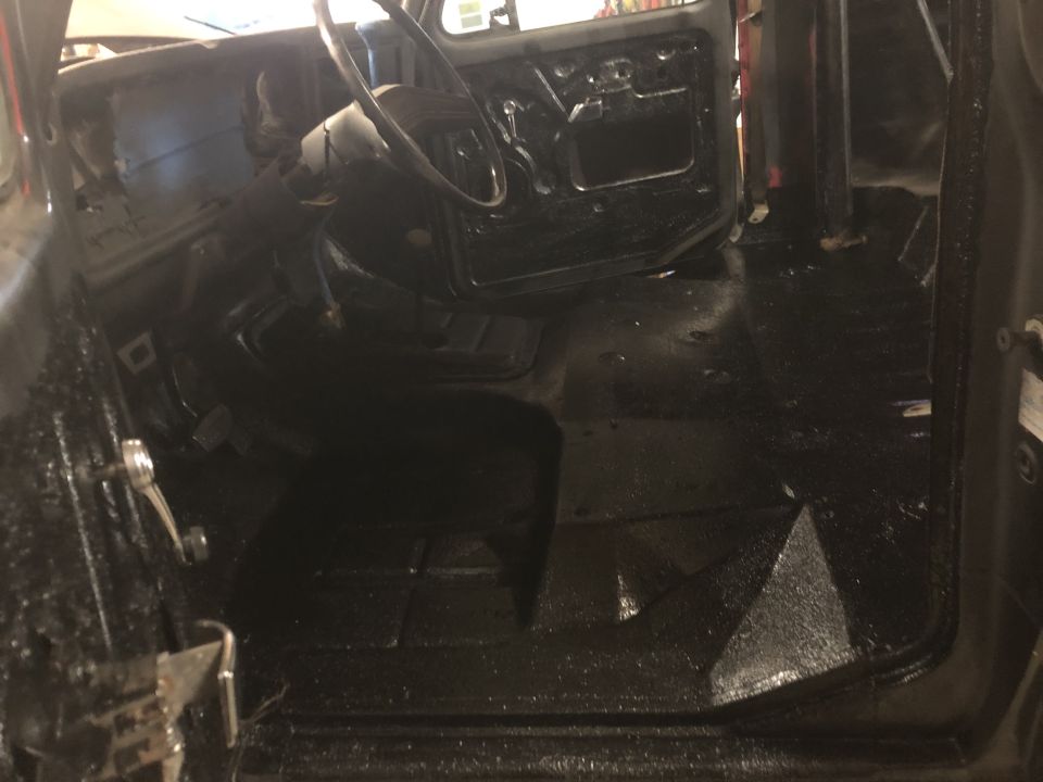 Interior view of a vehicle with black textured flooring and exposed door panels
