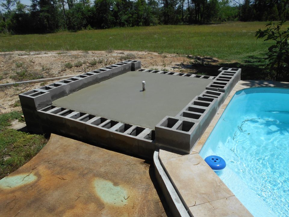 Concrete pool deck under construction with cinder blocks and fresh cement, next to a blue swimming pool