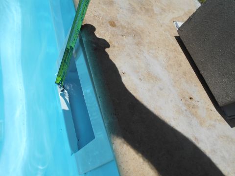 1992 Ford Bronco - A green measuring tape is used to measure the water depth at the edge of a swimming pool.