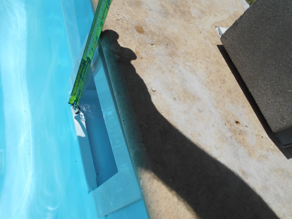 Pool edge with a green measuring tape showing water depth, concrete deck, and a dark shadow