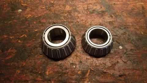 1985 Ford Bronco - Two tapered roller bearings are shown on a wooden surface, with one bearing being larger than the other.