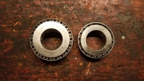 1985 Ford Bronco - Two tapered roller bearings are shown on a dark, weathered wooden surface. The larger bearing on the left is marked "TIMKEN USA 091760 HM88…