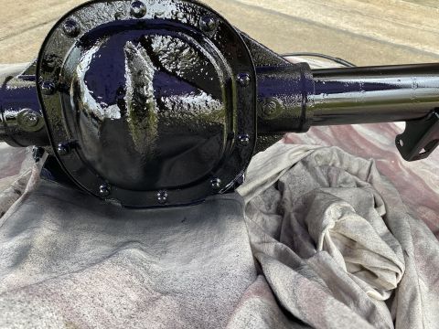 1994 Ford Bronco - A black painted differential housing and axle tube are shown resting on a gray cloth. The differential cover is round and secured with mult…