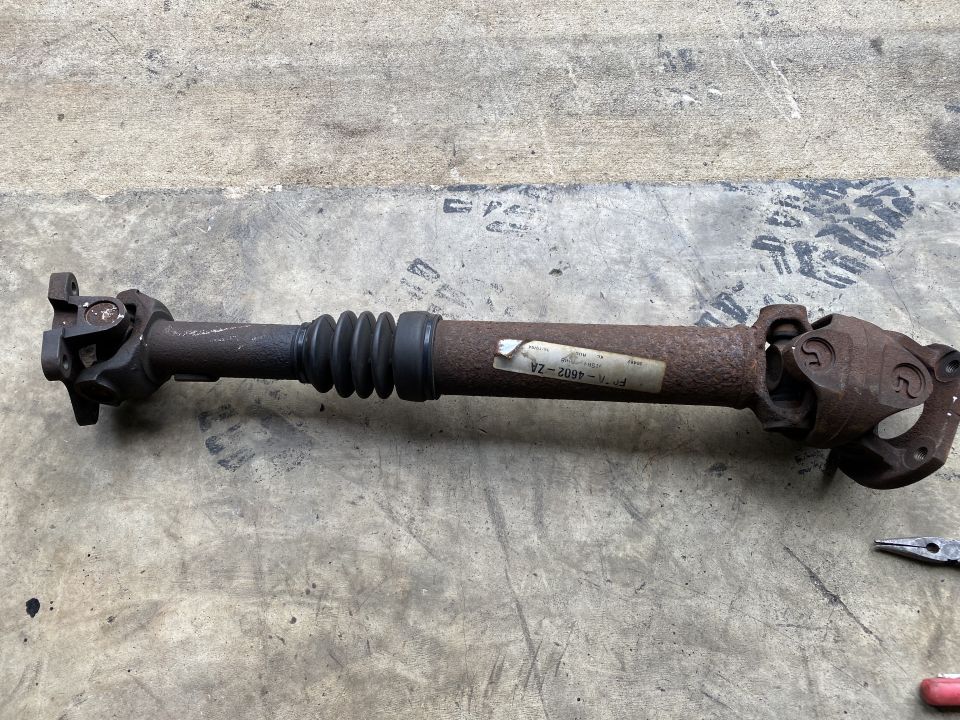 Rusty driveshaft with rubber boot and U-joints on concrete.