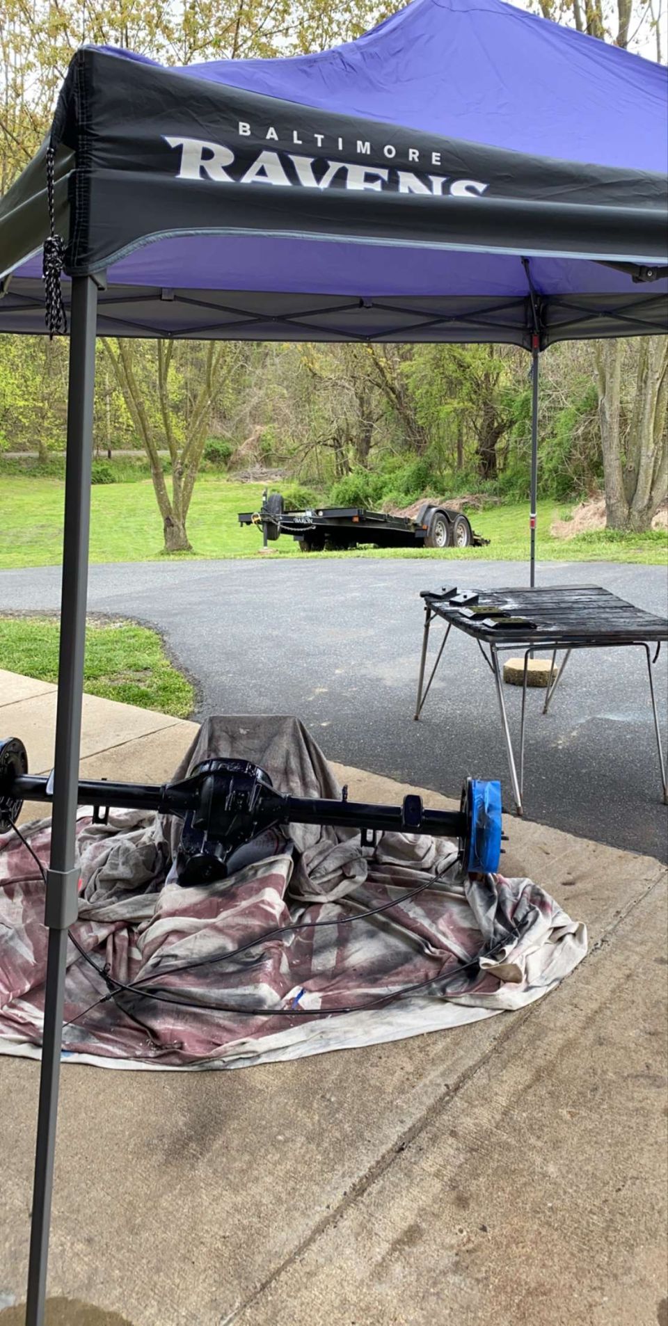 Black differential assembly on a tarp under a Baltimore Ravens canopy, utility trailer in background.