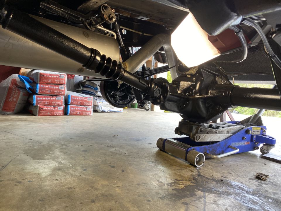 Underside of a vehicle showing rear differential and driveshaft on a jack.