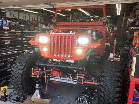 1992 Jeep Wrangler - A custom orange Jeep Wrangler is parked in a garage with its hood open, showcasing its engine and large off-road tires. The vehicle is supp…