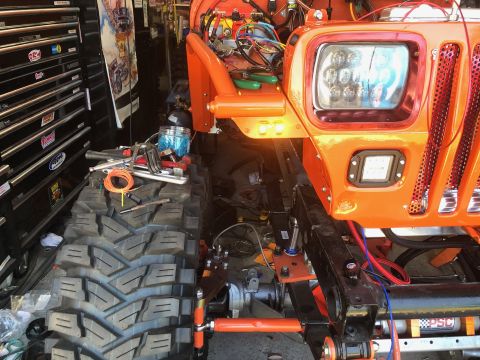1992 Jeep Wrangler - A bright orange Jeep Wrangler is shown with its front end partially disassembled, revealing wiring and suspension components. Tools and a l…