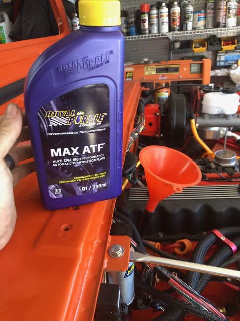 1992 Jeep Wrangler - A person's hand holds a bottle of Royal Purple Max ATF synthetic oil over the engine bay of an orange vehicle. A red funnel is placed into…