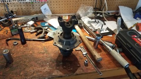 1985 Ford Bronco - A differential gear set and associated tools are laid out on a wooden workbench. Visible tools include a torque wrench, hammer, crowbar, an…