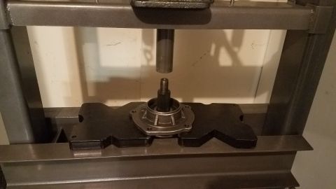 1985 Ford Bronco - A metal shaft is positioned above a vehicle hub assembly held in a hydraulic press. The hub assembly is mounted on a black metal support wi…