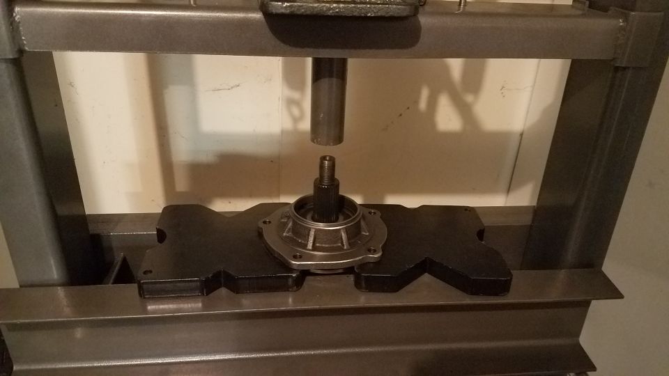 Vehicle hub assembly in a hydraulic press with a shaft above it.