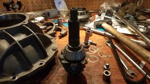 1985 Ford Bronco - A close-up view of automotive differential parts, including a ring gear with a bearing and pinion shaft, laid out on a wooden workbench wit…