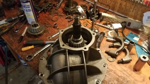 1985 Ford Bronco - A close-up view of a differential housing with a splined shaft and bearing assembly installed, surrounded by various tools and parts on a w…