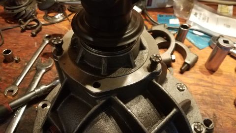 1985 Ford Bronco - A close-up view of a differential housing with several bolts being tightened with a wrench on a wooden workbench. Various tools and parts a…