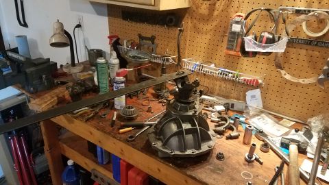1985 Ford Bronco - A workbench is cluttered with automotive parts, including a differential, tools, and cleaning supplies, suggesting a vehicle repair or buil…