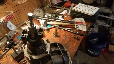 1985 Ford Bronco - A workbench is cluttered with tools and automotive parts, including a differential housing and a torque wrench. Various sockets, a hammer,…