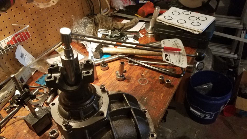 Workbench with automotive parts and tools including a differential, torque wrench, sockets, and hammer.