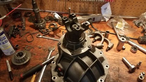 1985 Ford Bronco - A differential housing with a yoke attached sits on a wooden workbench surrounded by tools and parts, including a bearing, a spray can, and…