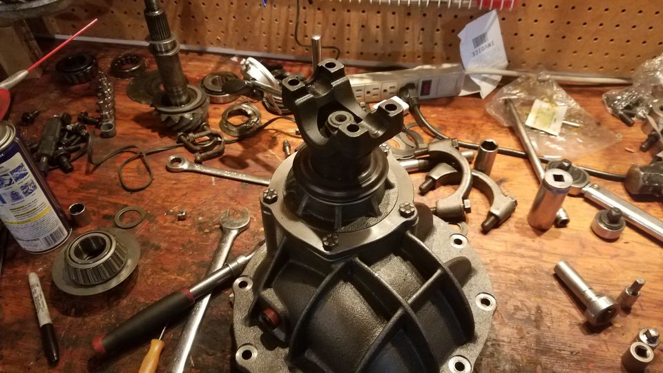 Differential housing with yoke, tools, and parts on a workbench.
