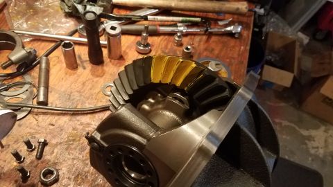 1985 Ford Bronco - A close-up view of a differential gear set with yellow marking compound on the teeth, resting on a wooden workbench alongside various tools…