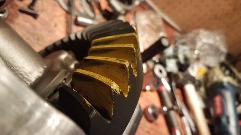 1985 Ford Bronco - A close-up, angled view of a black and yellow gear, likely a differential gear, showing wear marks on its teeth. The gear is part of a vehi…