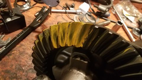 1985 Ford Bronco - A close-up view of a differential ring gear with yellow marking compound applied to its teeth, resting on a wooden workbench with various t…