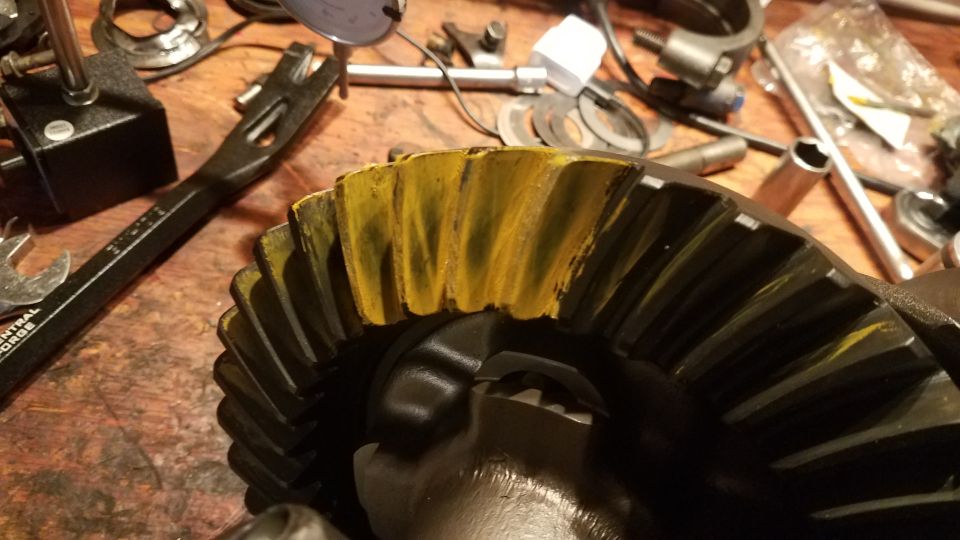 Differential ring gear with yellow marking compound on teeth, tools on workbench.