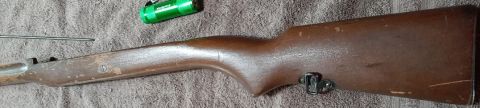2003 Ford F-250 - A wooden rifle stock is shown lying on a textured surface. A green flashlight and a metal rod are also visible in the image.