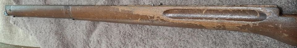Close-up of a worn wooden firearm stock with peeling finish.