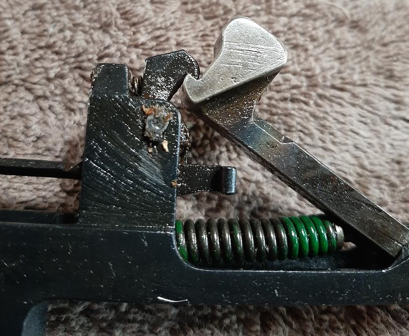 Close-up of firearm internal mechanism with black frame, silver lever, and green spring.