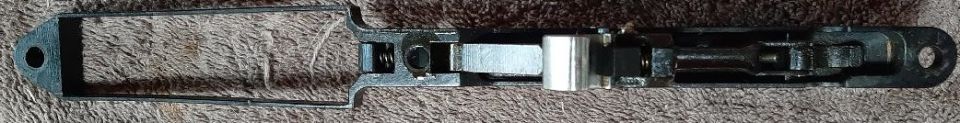 Disassembled firearm bolt carrier group on a textured brown surface.