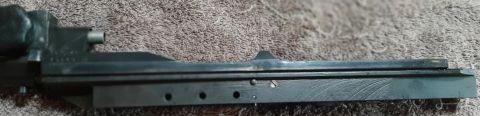 2003 Ford F-250 - This is a close-up, side-view photo of a metal firearm receiver on a textured brown surface.