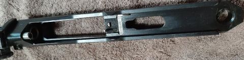 2003 Ford F-250 - A close-up, overhead view of a black metal firearm receiver, possibly from a rifle, resting on a textured brown surface.