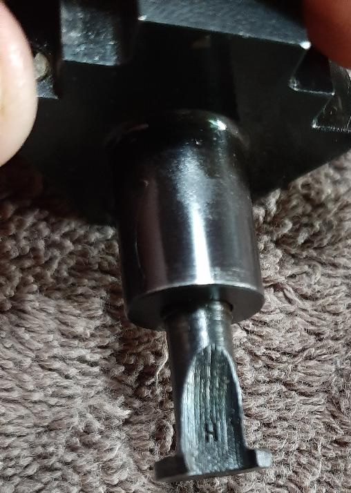 Close-up of a metal part with a slotted end on a textured surface.