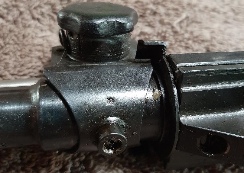 Close-up of a metal firearm component with a black knob and screw.