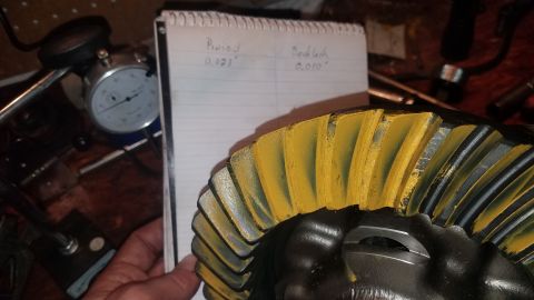 1985 Ford Bronco - A close-up view of a differential gear with yellow markings on its teeth. In the background, a notebook shows handwritten measurements for…