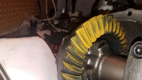1985 Ford Bronco - A close-up shows a differential gear with yellow marking compound applied to the teeth, indicating contact points. A notebook with handwrit…