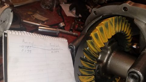 1985 Ford Bronco - A close-up view of a differential gear set with yellow marking compound on the teeth. A notepad in the foreground shows handwritten measure…