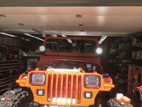 1992 Jeep Wrangler - Front view of an orange Jeep Wrangler with aftermarket LED headlights and auxiliary lights mounted on the fenders. The vehicle is in a gara…