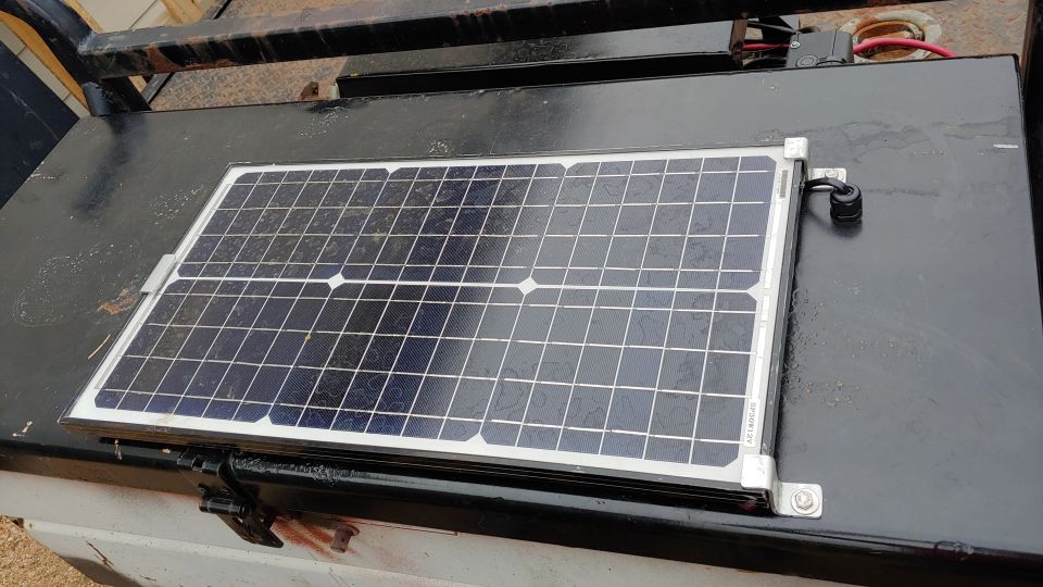 Small solar panel bolted to a black metal toolbox with red and black wiring visible