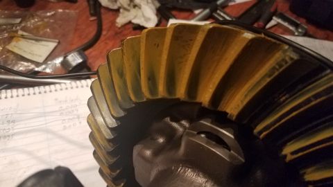 1985 Ford Bronco - A close-up view of a ring gear with yellow and black teeth, possibly from a differential. A notebook with handwritten measurements is visib…