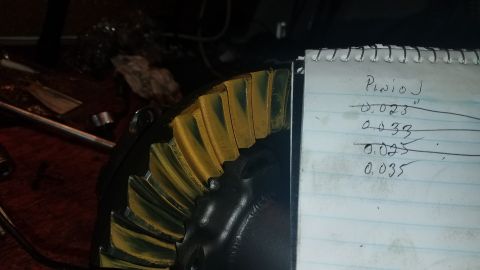 1985 Ford Bronco - A close-up view of a differential ring gear with yellow marking compound applied to its teeth, next to a notepad with handwritten measureme…