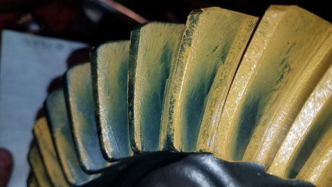 1985 Ford Bronco - A close-up, angled view shows the teeth of a yellow and teal painted gear, likely a differential gear, with visible wear marks on the teeth.